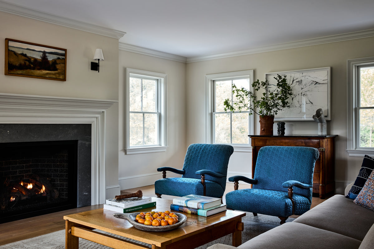 Paired antique armchairs at a brick fireplace below a landscape painting, Martin & Brockett Hudson Valley