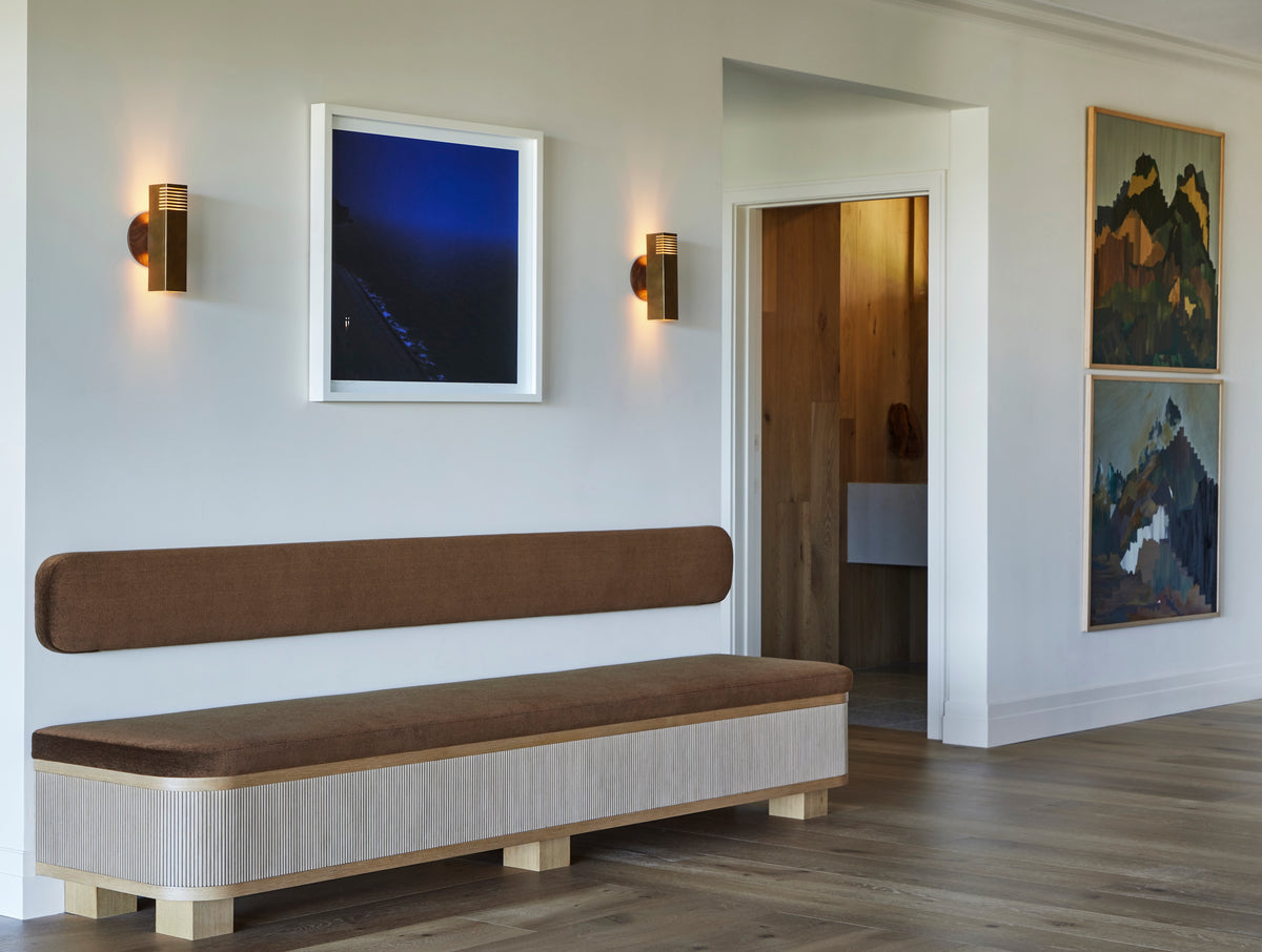 Upholstered bench with a fluted base below blue artwork and sconces, Martin & Brockett San Rafael entry