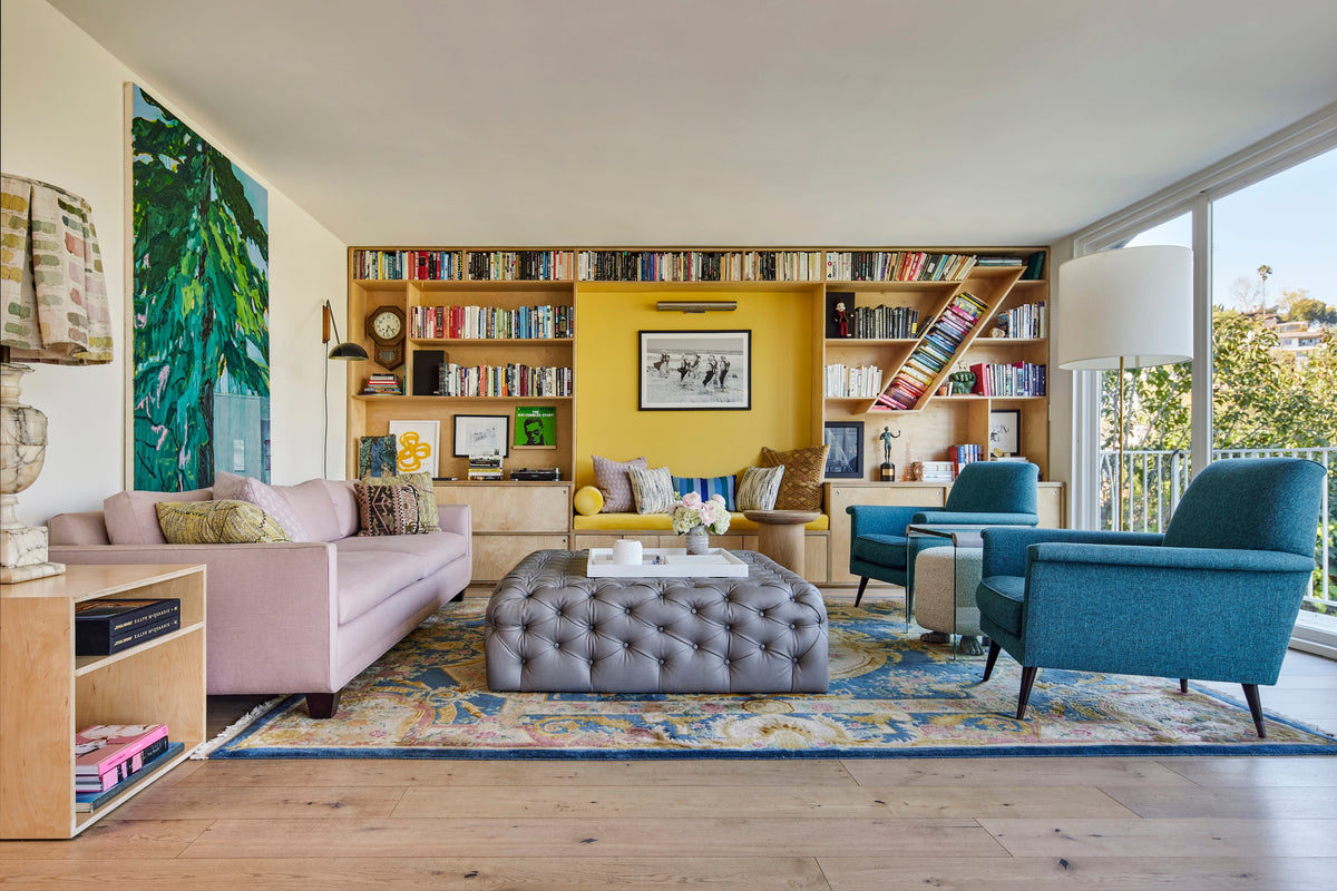 Oak bookshelf wall with a library ladder above a mauve sofa and tufted ottoman, Martin & Brockett Silverlake